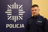 zdjęcie przedstawia dzielnicowego Marcina Kopcia. Obok niego stoi policyjny baner, na którym znajduje się policyjna gwiazda, a pod nią napis Policja