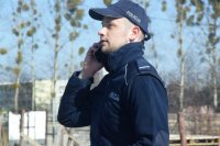 Na fotografii widać policjanta, który rozmawia przez telefon komórkowy.