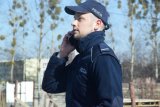 Na fotografii widać policjanta, który rozmawia przez telefon komórkowy.