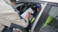 na fotografii widać mężczyznę, który stoi przy policyjnym radiowozie i podpisuje mandat karny