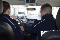 fotografia kolorowa: wnętrze radiowozu. Na przednich fotelach siedzą policjanci