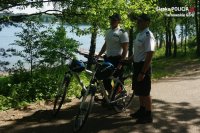 fotografia kolorowa: dwóch policjantów stoi obok policyjnych rowerów. W tle zdjęcia widać zalew