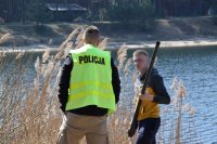 fotografia kolorowa: policjant rozmawia z wędkarzem. W tle widać zalew