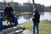 fotografia kolorowa: policjant rozmawia z wędkarzem, który schodzi z kładki. W tle widać zalew