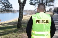fotografia kolorowa: policjant stoi na koronie zalewu i obserwuje plażę. Na plaży widać dwie osoby.