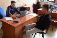 fotografia kolorowa: przy biurku siedzi policjant, który przesłuchuje podejrzanego  siedzącego po drugiej stronie biurka