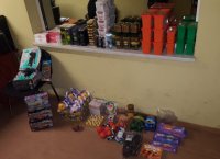 fotografia kolorowa: w pomieszczeniu na podłodze oraz krzesłach i parapecie stoją poukładane produkty spożywcze, chemiczne oraz zabawki
