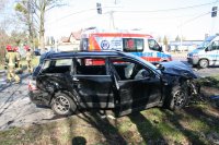 fotografia kolorowa: widać na niej bok rozbitego samochodu osobowego. W aucie są powybijane szyby, wystrzelone poduszki powietrzne. W tle zdjęcia widać karetkę pogotowia oraz policyjny radiowóz