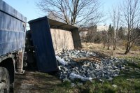 fotografia kolorowa: na zdjęciu widać przewróconą przyczepę, z której do przydrożnego rowu wysypała się kostka brukowa