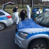 na fotografii widać policyjne radiowozy, obok których policjanci zakładają kombinezony ochronne