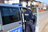fotografia kolorowa: policyjny radiowóz. Od strony pasażera, przy drzwiach, stoi policjant