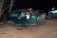 na zdjęciu widać zniszczony samochód osobowy, który znajduje się w przydrożnym rowie. Obok samochodu widać policyjny radiowóz i policjanta