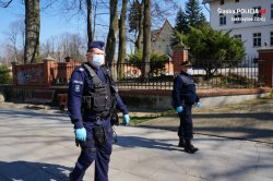 Na zdjęciu widać idących ulica policjanta i strażnika miejskiego, ubranych w maseczki i jednorazowe rękawice
