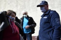 fotografia kolorowa: policjant wręczył maseczkę kobiecie, która zakłada ją na twarz