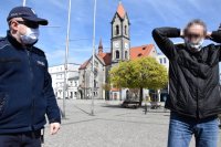 fotografia kolorowa: plac tarnogórskiego Rynku, na którym stoją policjant i mężczyzna, który zakłada na twarz otrzymaną od policjanta maseczkę
