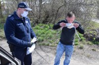 fotografia kolorowa: policjant przekazuje maseczkę mężczyźnie, który zakłada ją na twarz