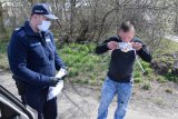 fotografia kolorowa: policjant przekazuje maseczkę mężczyźnie, który zakłada ją na twarz