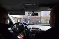 fotografia kolorowa: wnętrze radiowozu, w którym jadą dwaj policjanci