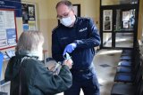 fotografia kolorowa: policjant przekazuje seniorce maseczki ochronne