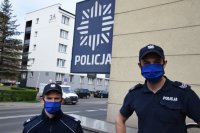 fotografia kolorowa: dwóch policjantów ubranych w maseczki ochronne. w tle widać bliki i zaparkowane samochody
