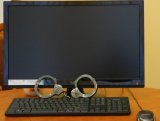 Na fotografii widać monitor komputera. Przed nim znajduje się klawiatura, na której leżą policyjne kajdanki