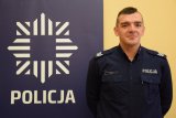 dzielnicowy sierż. szt. Szymon Łazaj stoi obok policyjnego baneru