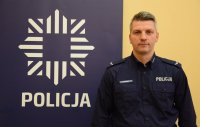 fotografia kolorowa; obok policyjnego baneru widać sierż. Pawła Syrnika