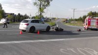 fotografia kolorowa: droga, na której widać przewrócony motocykl i stojący obok niego, samochód osobowy. Z prawej strony zdjęcia widać wóz strażacki, a z lewej policyjny radiowóz.