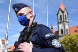 Fotografia kolorowa: policjant w maseczce. W tle fotografii widać budynki znajdujące się na tarnogórskim Rynku