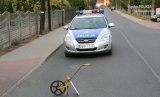 Na fotografii widać drogę, na środku której znajduje się policyjny radiowóz. Przed radiowozem, na jezdni widać przyrząd do pomiarów odległości.