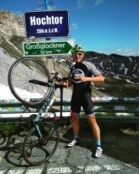 Kolarz trzyma rower na jednym kole, w tle rozciąga się widok pasma górskiego