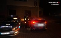 Na fotografii widać zaparkowany policyjny radiowóz oraz policjanta kontrolującego kierowcę samochodu osobowego