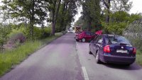 fotografia kolorowa: droga, przy której po obydwu stronach widać drzewa i pola. Z prawej strony zdjęcia, przy krawędzi drogi, widać samochody osobowe, policyjny radiowóz oraz pomoc drogową.