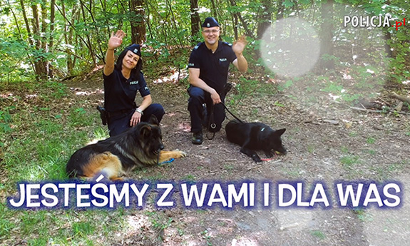 Na zdjęciu widać policjantkę i policjanta, którzy siedzą obok policyjnych psów. Tekst na zdjęciu Jesteśmy z Wami i dla Was
