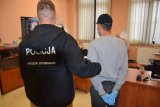 fotografia kolorowa: policjant prowadzi zatrzymanego mężczyznę.