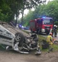 Na zdjęciu widać rozbity samochód osobowy, który leży na dachu. Nieopodal samochodu widać strażaków, policjantów oraz wóz strażacki i policyjne radiowozy.