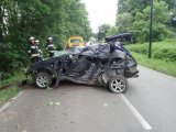 Na fotografii widać kompletnie rozbity samochód osobowy, który stoi na ulicy po wyciągnięciu z rowu. Obok wraku samochodu stoją strażacy
