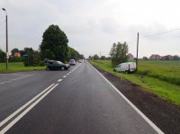 Droga, na której widać rozbity samochód osobowy i stojący za nim policyjny radiowóz. Z prawej strony zdjęcia widać, jak w przydrożnym rowie stoi inny rozbity samochód