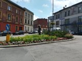 Na fotografii widać zielone rondo, dookoła którego znajdują się budynki i samochody