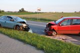 Na fotografii widać drogę, na której stoją dwa samochody osobowe. Pojazdy mają zniszczony przód, po czołowym zderzeniu