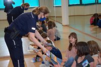 fotografia kolorowa: policjanta rozdaje ulotki siedzącym na podłodze dzieciom.