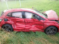 Na fotografii widać bok zniszczonego samochodu osobowego, który stoi w przydrożnym rowie