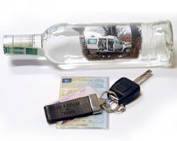 Zdjęcie przedstawia pustą butelkę po alkoholu, dowód rejestracyjny od pojazdu oraz leżące na nim kluczyki od samochodu.
