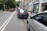 na fotografii widać ulicę Sobieskiego w Tarnowskich Górach, na której widać uszkodzone samochody biorące udział w wypadku, policyjne radiowozy, wozy strażackie oraz inne samochody. Po obydwu stronach drogi, na chodniku widać osoby.