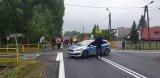 Na fotografii widać skrzyżowanie, na którym po przejściu dla pieszych przemieszcza się duża grupa osób z transparentami. Przed nimi w poprzek drogi stoi policyjny radiowóz i policjant