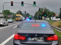 Na fotografii widać skrzyżowanie, na którym znajdują się samochody ciężarowe i osobowe. Na jednym z pasów stoi nieoznakowany radiowóz policyjny, który wyświetla napis &quot;OBJAZD&quot;