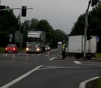 Na fotografii widać skrzyżowanie, na którym znajdują się samochody ciężarowe i osobowe. Na skrzyżowaniu policjant kieruje ruchem.
