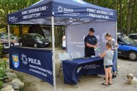 policjant w namiocie informacyjnym rozdaje ulotki i rozmawia z osobami