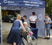 osoba niepełnosprawna na wózku z opiekunem stoi przed namiotem informacyjnym gdzie stoi dwóch policjantów