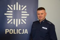 zdjęcie przedstawia dzielnicowego stojącego obok baneru, na którym widnieje policyjna gwiazda i napis Policja